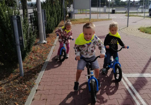 dzieci jadą na rowerkach biegowych