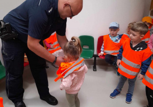 Pon policjant zakłada dzieciom kamizelki odblaskowe