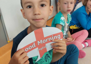 chłopiec pokazuje kartę z napisem dzień dobry po angielsku