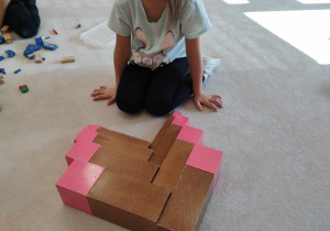 dziewczynka układa brązowe schody i różową wieżę