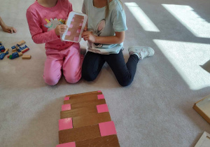 dziewczynki układą brązowe schody i różową wieżę