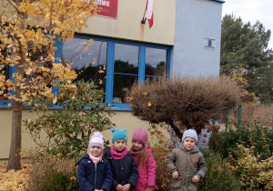 grupa przedszkolaków prezentuje na budynku przedszkola flagę i godło Polskii