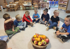 dzieci siedzą wokół kosza z warzywami i owocami