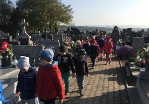 Dzieci idą alejkami cmentarza