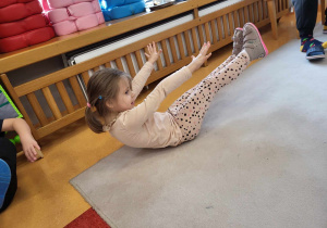 dziewczynka siedzi na dywanie bez dotykania rąk i nóg