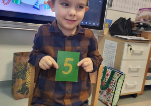 chłopiec trzyma tabliczkę z cyfrą pięć