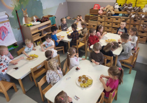 dzieci siedzą przy stolikach i jedzą poczęstunek od Franusia