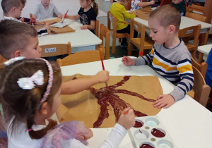 przedszkolaki malują farbami konary drzew