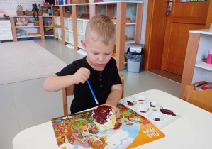 chłopiec maluje farbą kulkę z papieru