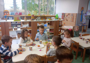 dzieci siedzą przy stolikach podczas poczęstunku