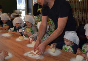 pan Krzysztof pokazuje dzieciom w jaki sposób formowa ciasto do pizzy