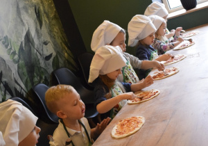 dzieci rozsmarowują sos pomidorowy na pizzy