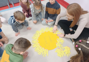 Pani nakleja wycięte dłonie, tworząc słoneczko