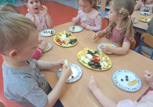 Dzieci wybierają owoce i układają na swoje talerzyki