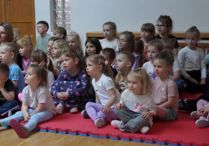 dzieci siedzą na piankach i oglądają przedstawienie