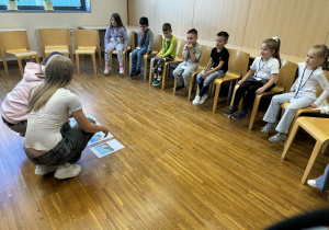 dzieci siedzą w pólkolu na krzesełkach i słuchaja poleceń uczenic