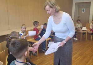 Pani nauczycielka jezyka angielskiego wręcza dzieciom karty pracy i podaje im ręke