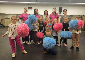 grupowe zdjęcie gdzie dzieci trzymaja pompony wraz z paniami z grupy i cheeleaderkami