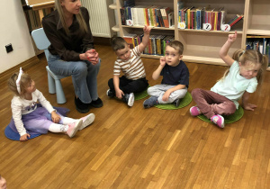 dzieci siedzą na dywanikach w bibliotece