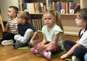 dzieci siedzą na dywanikach w bibliotece