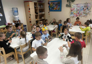 Dzieci siedzą przy stolikach i jedzą batony