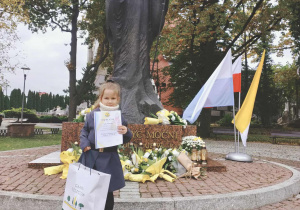 Dziewczynka pozuje z dyplomem pod pomnikiem Papieża