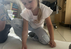 Dziewczynka układa na dywaniku odpowiednią ilość kasztanów