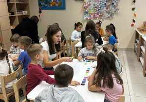 Dzieci siedzą przy stolikach z licealistami