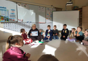 dzieci siedzą w kole, nauczyciel pokazuje plakat projektu "Mali odkrywcy Wielkiej Brytanii"