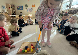 dziewczynka trzyma chwytak i wyciąga z worka owoc