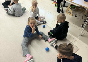 dzieci siedzą w parach, twarzą do siebie a pomiędzy nimi jest mała plastikowa piłka