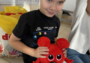 hłopiec karmi czerwonego potworka maskotkę owocem według polecnia nauczyciela