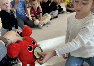 dziewczynka karmi czerwonego potworka maskotkę owocem według polecnia nauczyciela