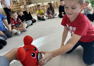 chłopiec karmi czerwonego potworka maskotkę owocem według polecnia nauczyciela