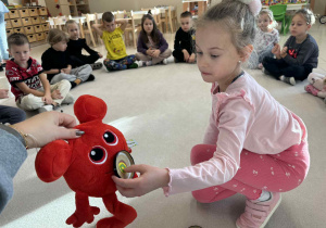 dziewczynka karmi czerwonego potworka maskotkę owocem według polecnia nauczyciela