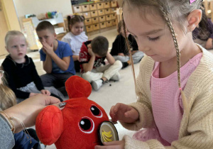 dziewczynka karmi czerwonego potworka maskotkę owocem według polecnia nauczyciela