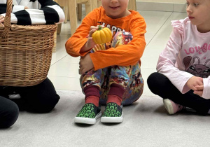 chłopiec siedzi w kole i trzyma w dłoni wyciągnietą z koszyka dynię