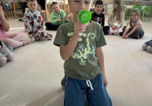 chłopiec siedzi w środku koła i trzyma megafon zmiejący głos i wypowiada nazwe owocu w j.angielski