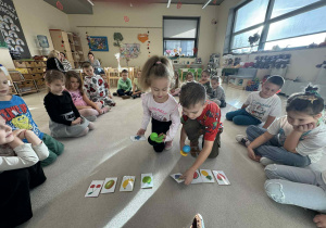 chłopiec i dziewczynka trzymają w dłoni platikowe łyzki z plasikowymi jajkami i kładą na odpowiedni owoc według polecenia nauczyciela