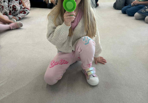 dziewczynka siedzi w środku koła i trzyma megafon zmiejący głos i wypowiada nazwe owocu w j.angielskim