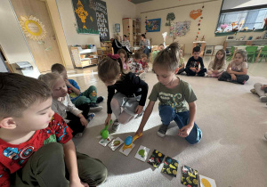chłopiec i dziewczynka trzymają w dłoni platikowe łyzki z plasikowymi jajkami i kładą na odpowiedni owoc według polecenia nauczyciela