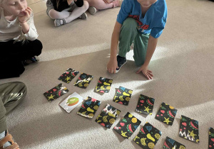 chłopiec siedzi w kole i odkrywa karty do gry memory owoce