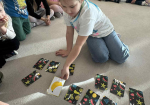 dziewczynka siedzi w kole i odkrywa karty do gry memory owoce