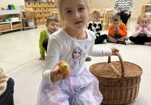 dziewczynka siedzi i trzyma koszyk a w drugiej ręce kolbę kukurydzy