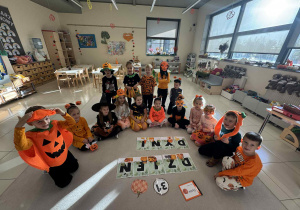 dzieci siedzą w półkolu ubrane w dyniowe stroje i pomiędzy nimi jest napis "dzień dyni"