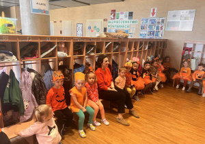 dzieci z najmłoszej grupy wraz z pania siedzą na ławce w dyniowych strojach