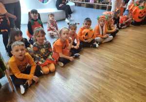 dzieci siedzą na podłodze w strojach dyniowych i pozują do zdjęcia