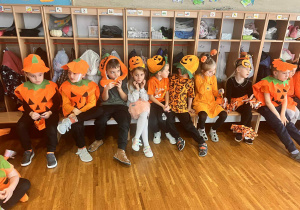 dzieci siedzą na ławce w dyniowych strojach i pozują do zdjęcia