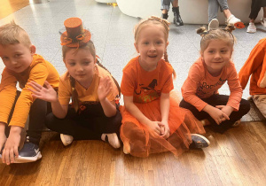 dzieci siedza na podłodze w pomarańczowych strojach