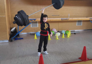 chłopiec jedną ręką pokazuje podnoszenie sztangi